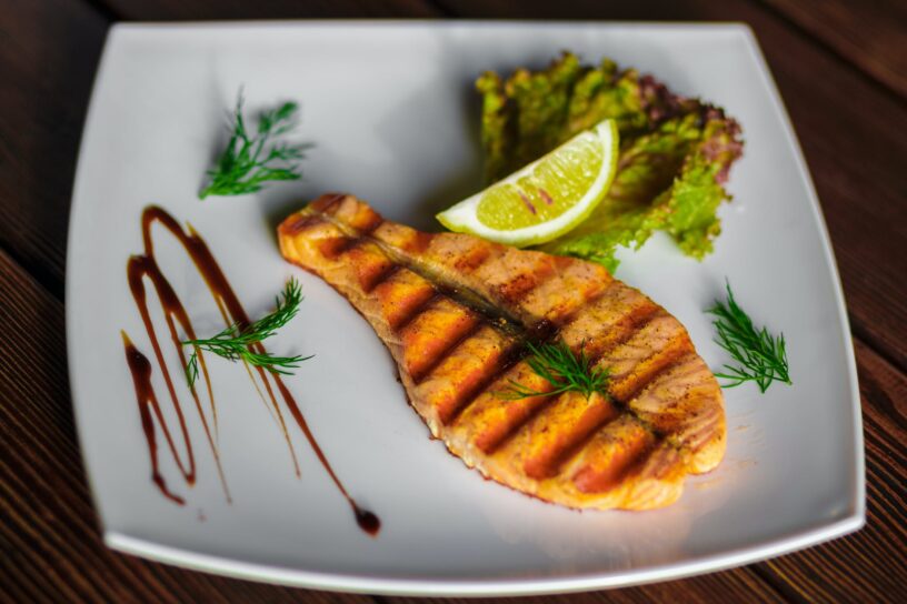 a slice of grilled fish and lime on a square ceramic plate